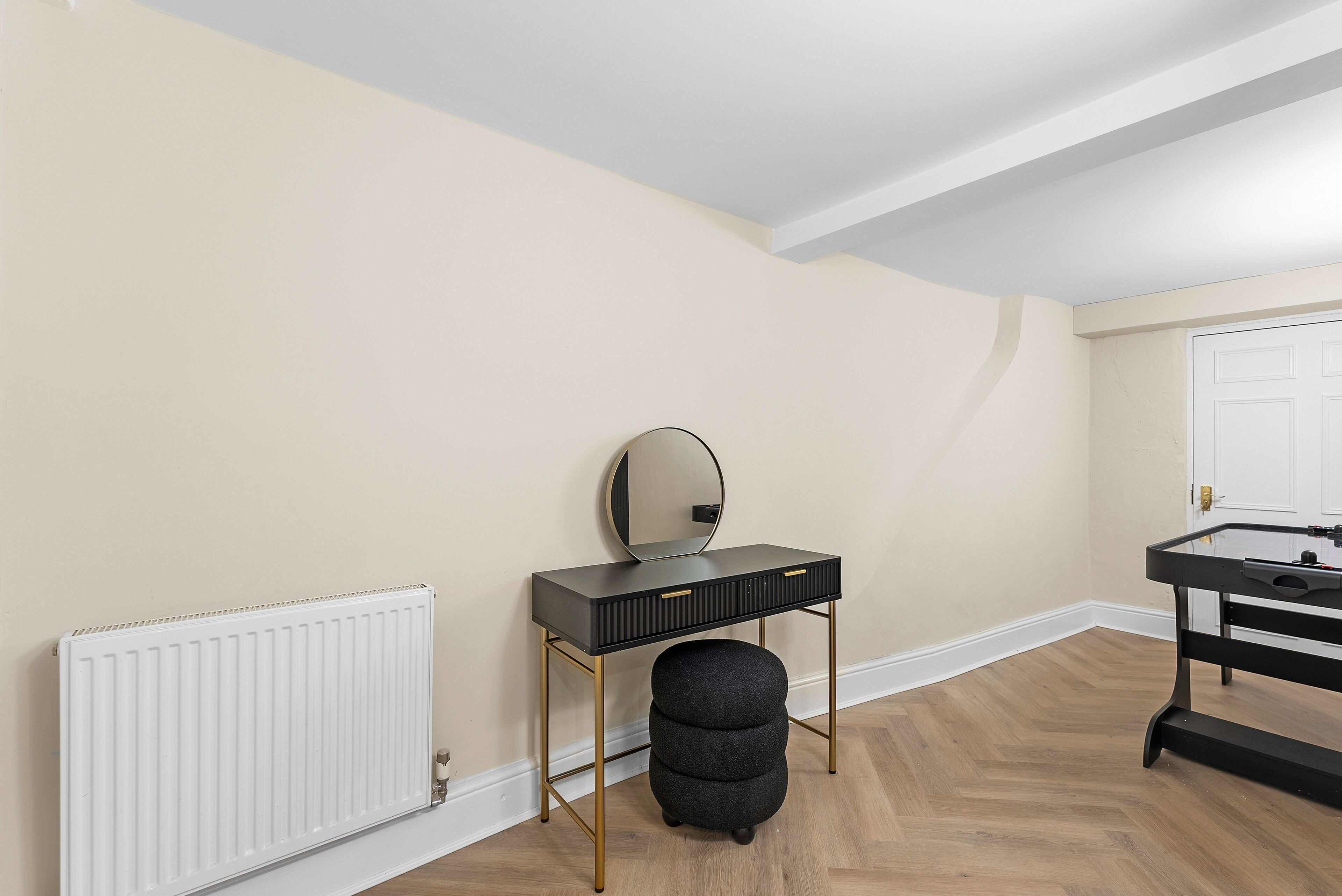 A room with a black vanity, a round mirror, a white radiator, and a black stool.