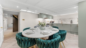 Un comedor moderno con una mesa redonda dispuesta para seis personas, rodeada de sillas tapizadas en color aguamarina con patas doradas.