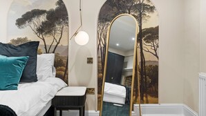Un dormitorio con cama, un banco, un espejo y un mural de árboles.