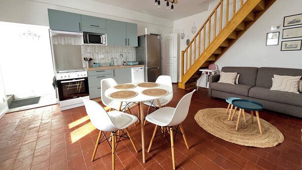 A modern kitchen with white cabinets, a microwave, and a refrigerator. There is a dining area with a round table and white chairs. A staircase leads to a living area with a sofa and a coffee table. - Le Palmier - Cosy gîte with all comforts (Chailles)