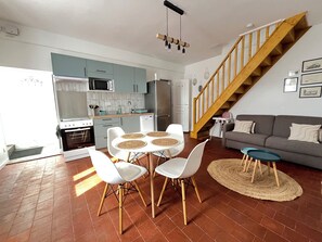 A modern kitchen with white cabinets, a microwave, and a refrigerator. There is a dining area with a round table and white chairs. A staircase leads to a living area with a sofa and a coffee table. - Le Palmier - Cosy gîte with all comforts (Chailles)