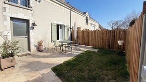 A patio with a table and chairs, a wooden fence, and a house with a chimney. - Le Palmier - Cosy gîte with all comforts (Chailles)