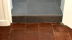A bathroom with dark grey tiles on the walls and a brown tiled floor. - Le Palmier - Cosy gîte with all comforts (Chailles)
