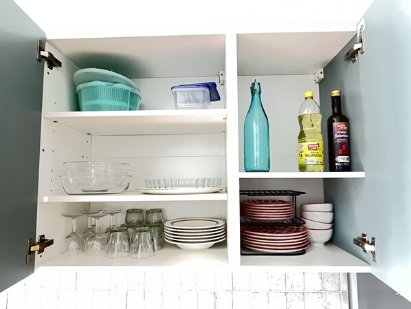 A kitchen with white cabinets, a glass bowl, wine glasses, plates, and bottles. - Le Palmier - Cosy gîte with all comforts (Chailles)