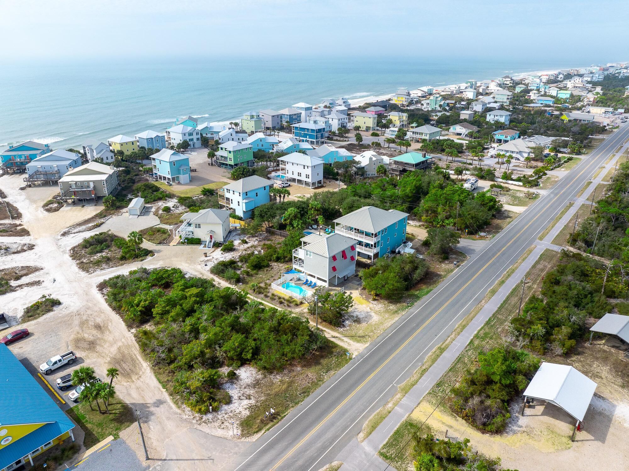 An aerial view of a coastal residential area with houses, a road, and a beach.