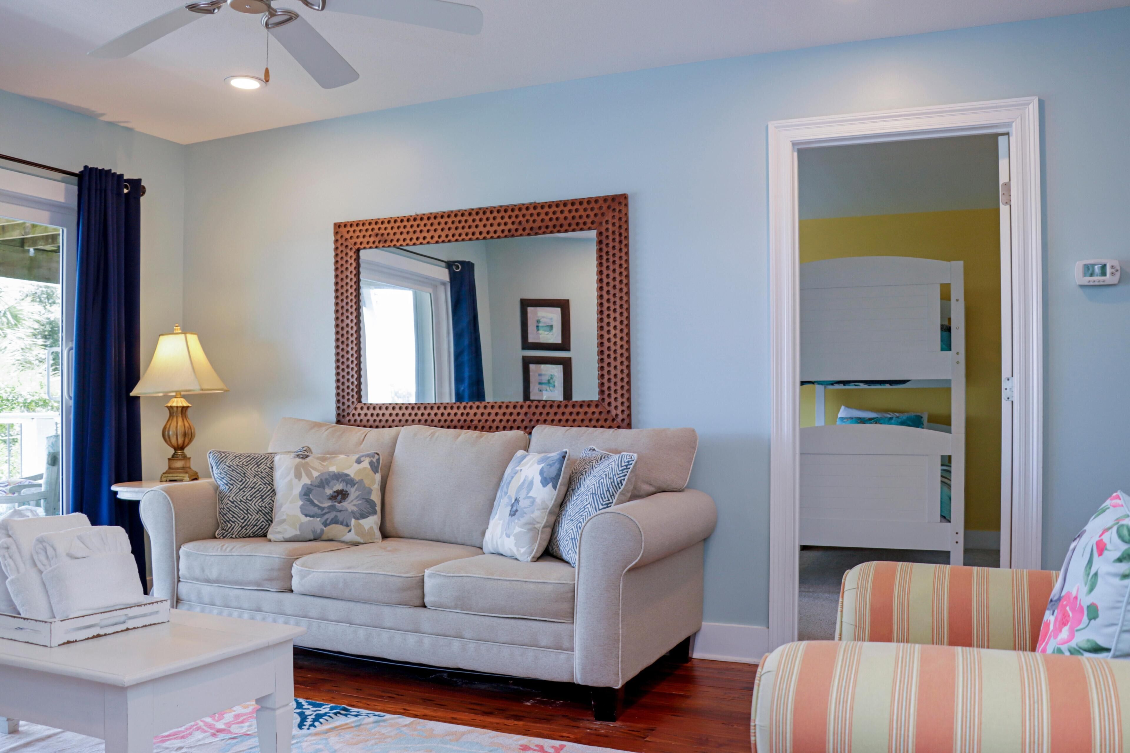 A living room with a sofa, a coffee table, a lamp, a mirror, and a door leading to a bedroom.