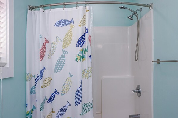 Baño con cortina de ducha de estampado de peces, una bañera blanca y un cabezal de ducha.