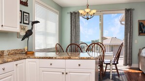 A kitchen with white cabinets, a granite countertop, and a dining area with wooden chairs.
