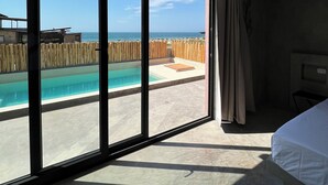 Habitación de hotel con un amplio ventanal corredero que da a una zona de piscina y vistas al mar.