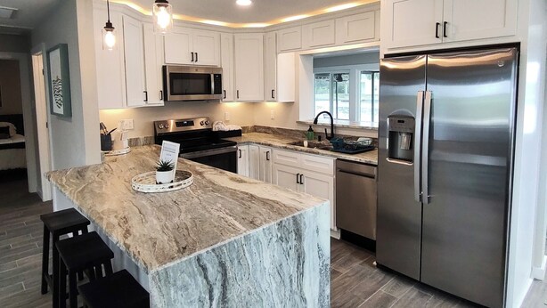 A modern kitchen with white cabinets, a stainless steel refrigerator, and a marble island with bar stools.