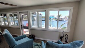 A room with a view of a marina, two blue armchairs, a patterned rug, and a ceiling fan.