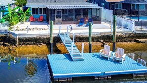 A dock with a blue deck, a pool, and a house with a covered patio.
