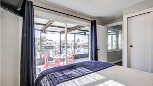 A bedroom with a bed, a large window, and a view of a balcony with chairs.