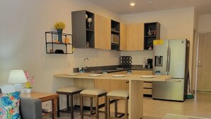 A modern kitchen with wooden cabinets, a stainless steel refrigerator, and a dining area with a blue table and chairs.