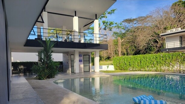 A modern building with a pool, a covered outdoor area, and a landscaped garden.
