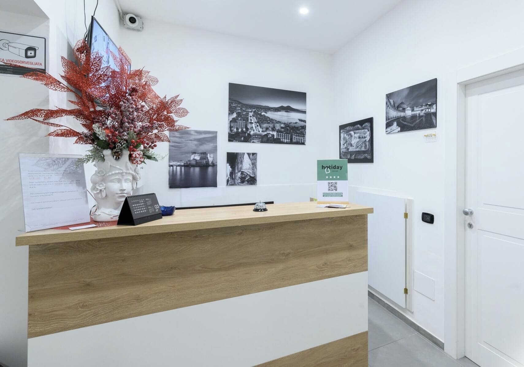 A reception desk with a wooden finish, a vase with red foliage, black and white photographs on the wall, and a 'hotday' sign.