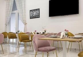Zona pranzo con tavoli, sedie e un televisore a schermo piatto appeso al muro.