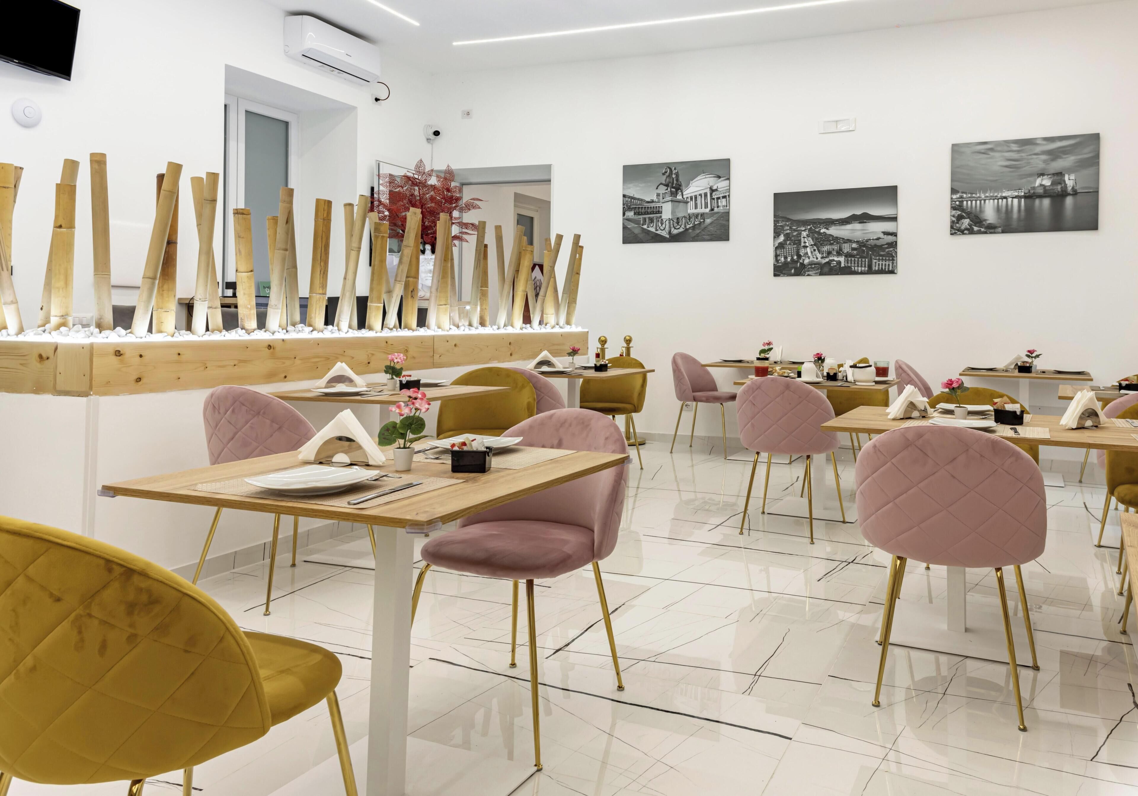 Ein Restaurant mit mehreren Tischen und Stühlen, einer dekorativen Bambusanordnung und schwarz-weißen Stadtansichten an der Wand.