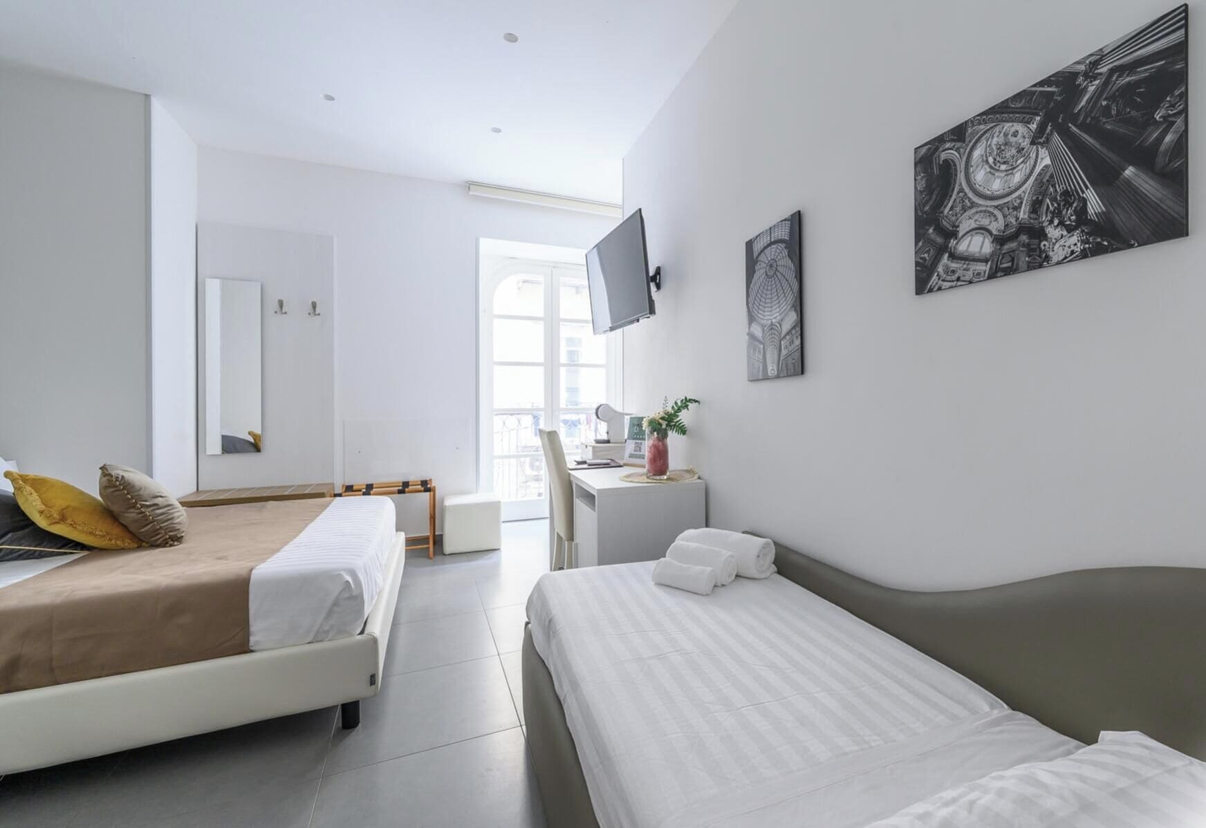 A modern hotel room with two beds, a desk, a flat-screen TV, and artwork on the walls.