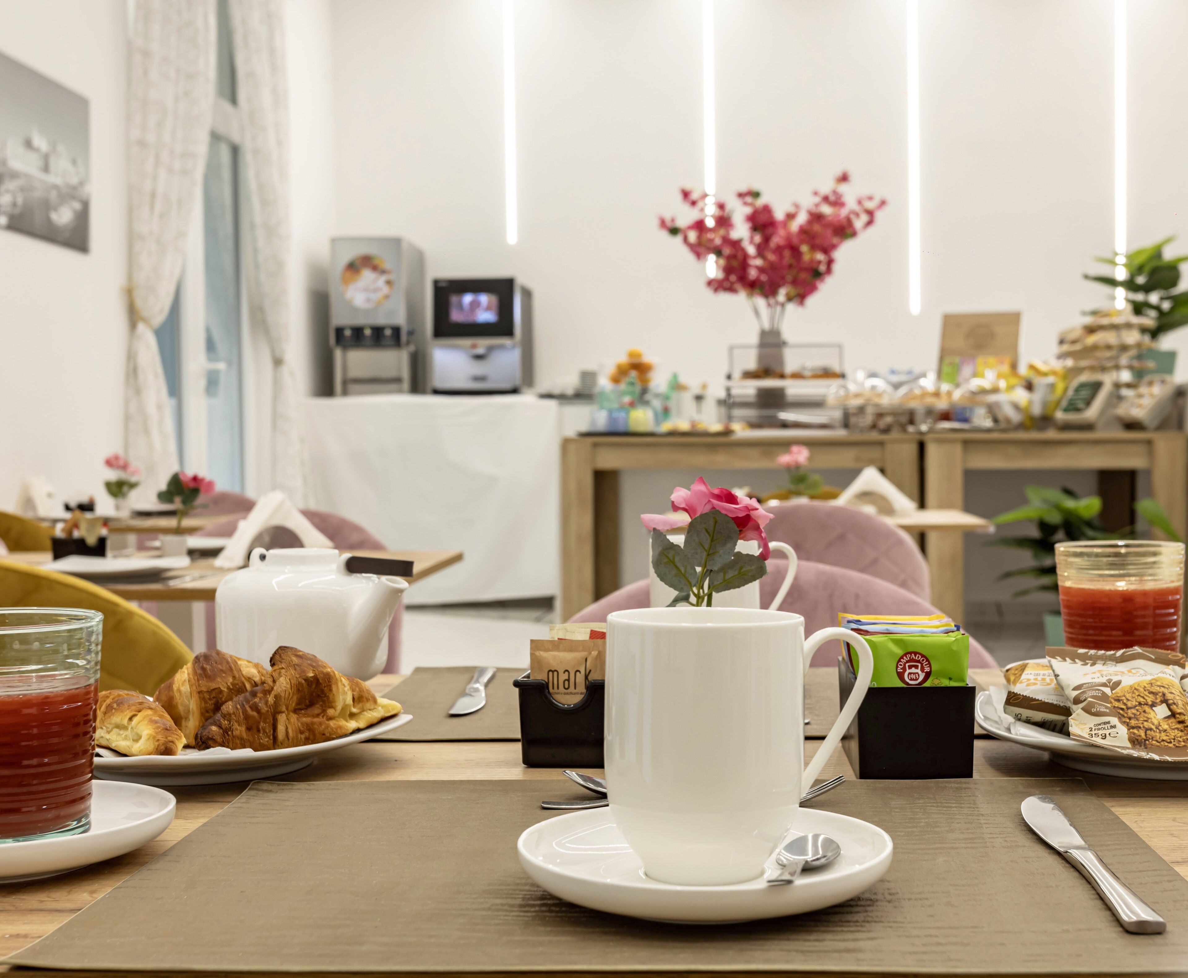 Et morgenbord med croissanter, en kop kaffe og en vase med blomster.
