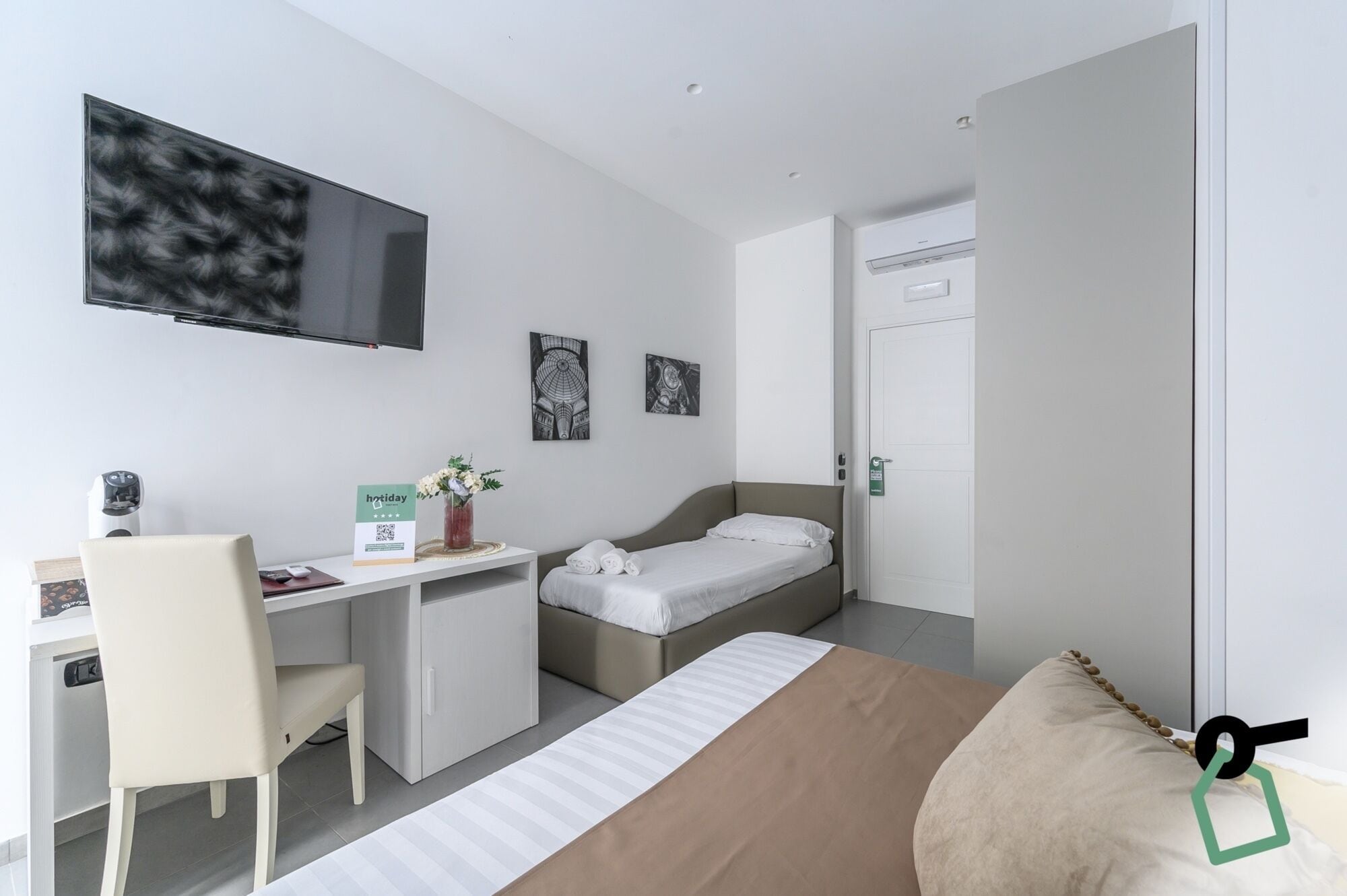 Een moderne hotelkamer met een bed, bureau, stoel en een wandgemonteerde flatscreen televisie.