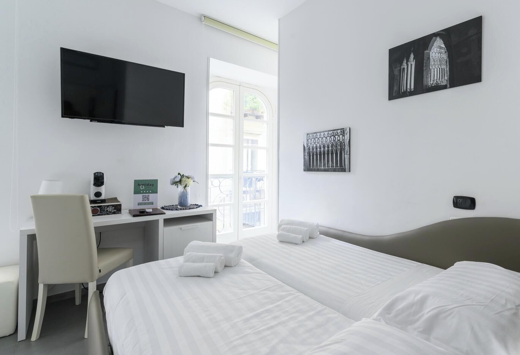 Ein Hotelzimmer mit einem Bett, einem Schreibtisch mit Computer, einem Fernseher und Kunstwerken an den Wänden.