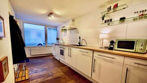Una cocina con armarios blancos, piso de madera, microondas y ventana con vista.