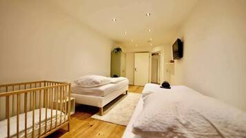 Ein Schlafzimmer mit einem Babybett, einem Bett, einem an der Wand montierten Fernseher und einer Tür zu einem anderen Raum.
