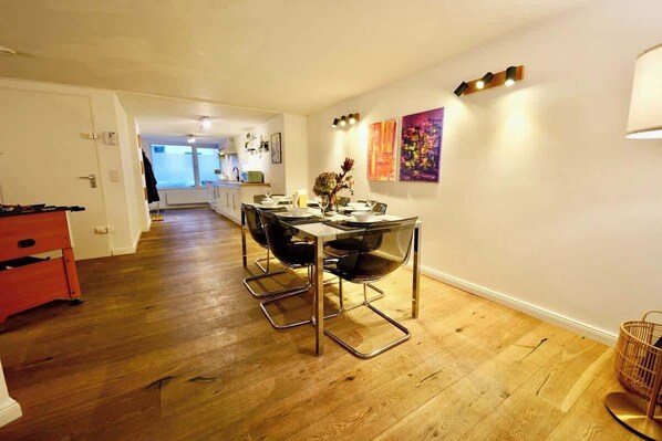 A dining area with a table set for four, a red sofa, and a kitchen in the background.
