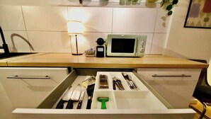 Una cocina con microondas, pileta y organizador de cajones con utensilios.