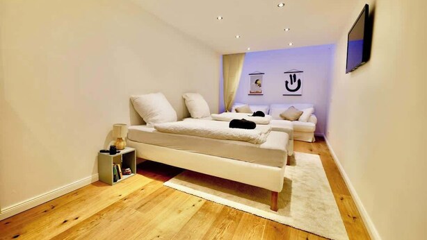 Un dormitorio moderno con una cama, una mesita de noche pequeña y un televisor en la pared.