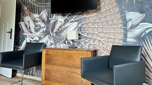 A room with a large wall mural, a flat-screen TV, two black leather chairs, and a wooden cabinet.