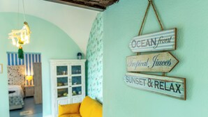 A room with a yellow sofa, a hanging light fixture, and a wall with signs reading "OCEAN front Tropical Juices Sunset & Relax". - Il Sogno, apartment with sea view in the historic center of Gaeta (Gaeta)