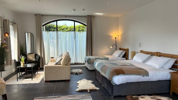 A modern bedroom with a large bed, a sofa, a desk, and a view of greenery outside. - The Jewel Lodge and Spa (Glengarriff)