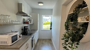 A narrow kitchen with a microwave, toaster, and coffee maker. There is a window with a view of greenery outside. - The Jewel Lodge and Spa (Glengarriff)