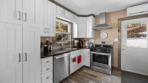 A modern kitchen with white cabinets, stainless steel appliances, and a large window.