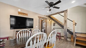 A dining area with a wooden table, white chairs, a ceiling fan, and a staircase with wooden steps.