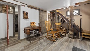 A rustic room with wooden flooring, a rocking chair, a vintage sewing machine, and a staircase with a wooden handrail.