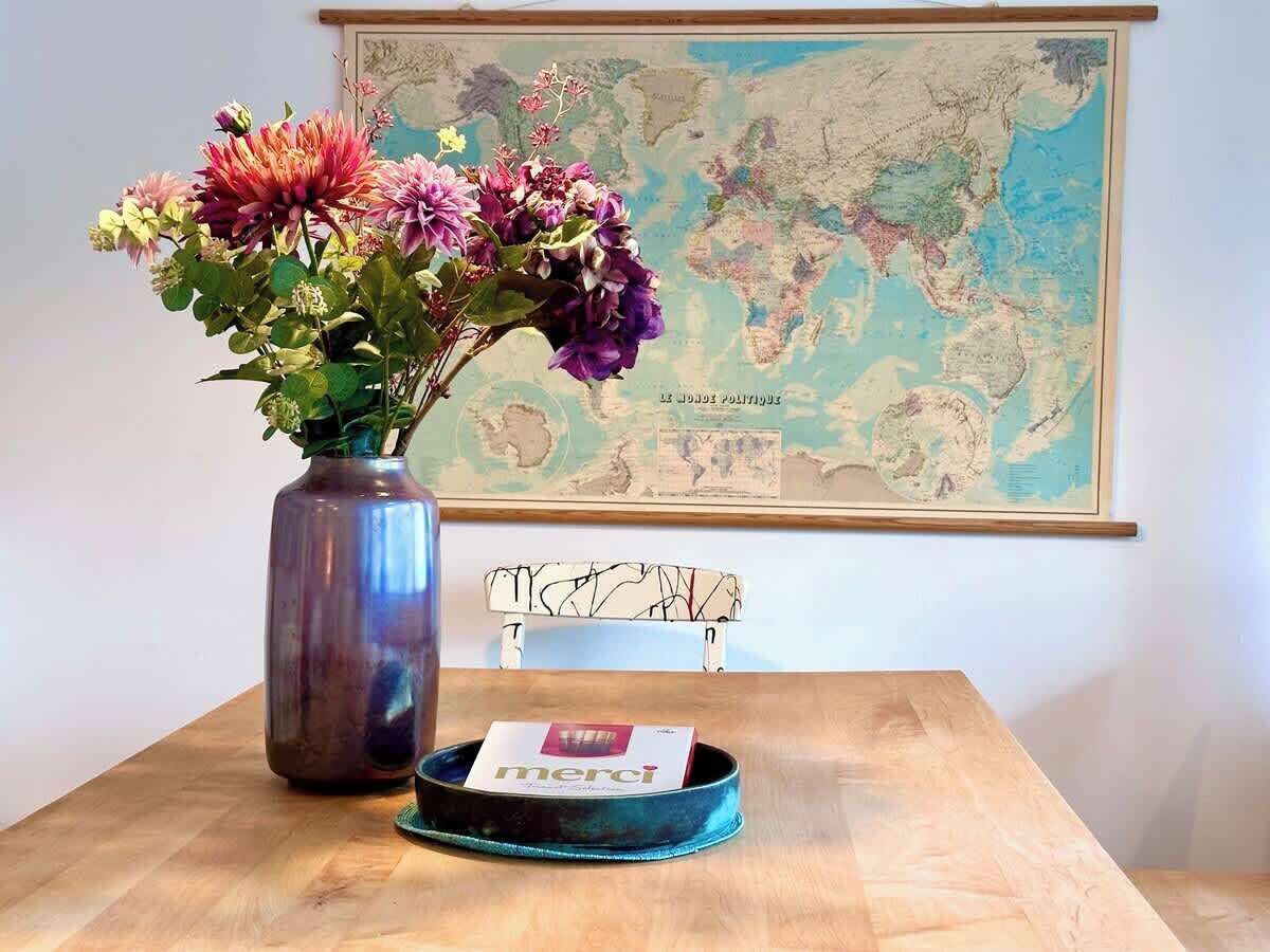 Ein Holztisch mit einem Blumenstrauß, einem Buch und einer Weltkarte an der Wand.