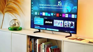 Un televisor de pantalla plana montado en un mueble blanco, con una interfaz digital que muestra varios canales y aplicaciones.