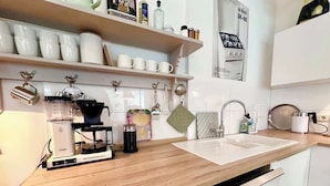 Una cocina con cafetera, un lavamanos y diferentes utensilios.
