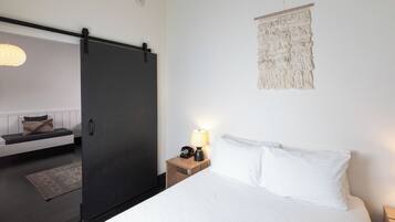 A bedroom with a bed, bedside table with a lamp, a wall hanging, and a sliding door leading to another room.