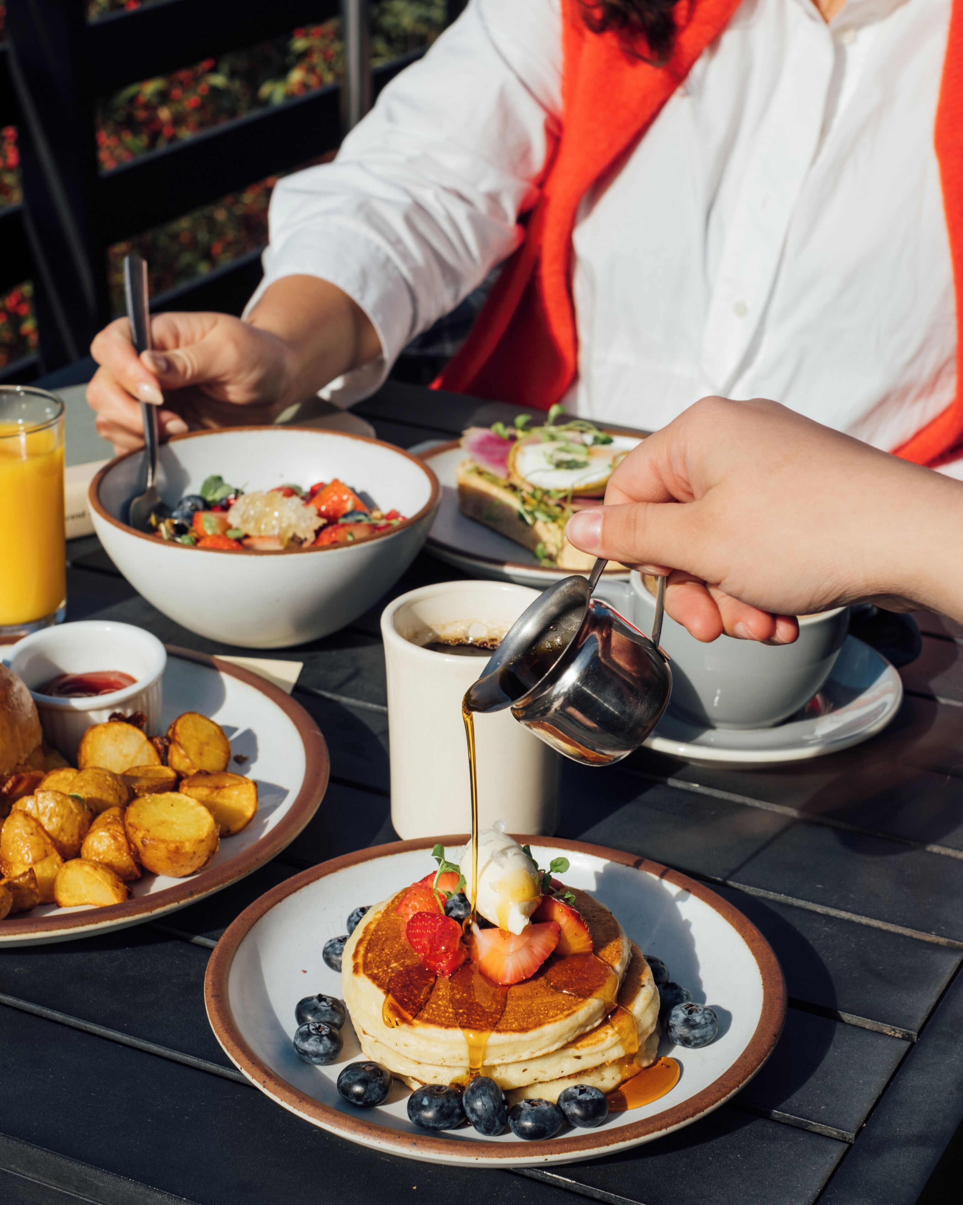 Desayuno con panqueques cubiertos de fresas, arándanos y jarabe, acompañado de una ensalada y un vaso de jugo de naranja.