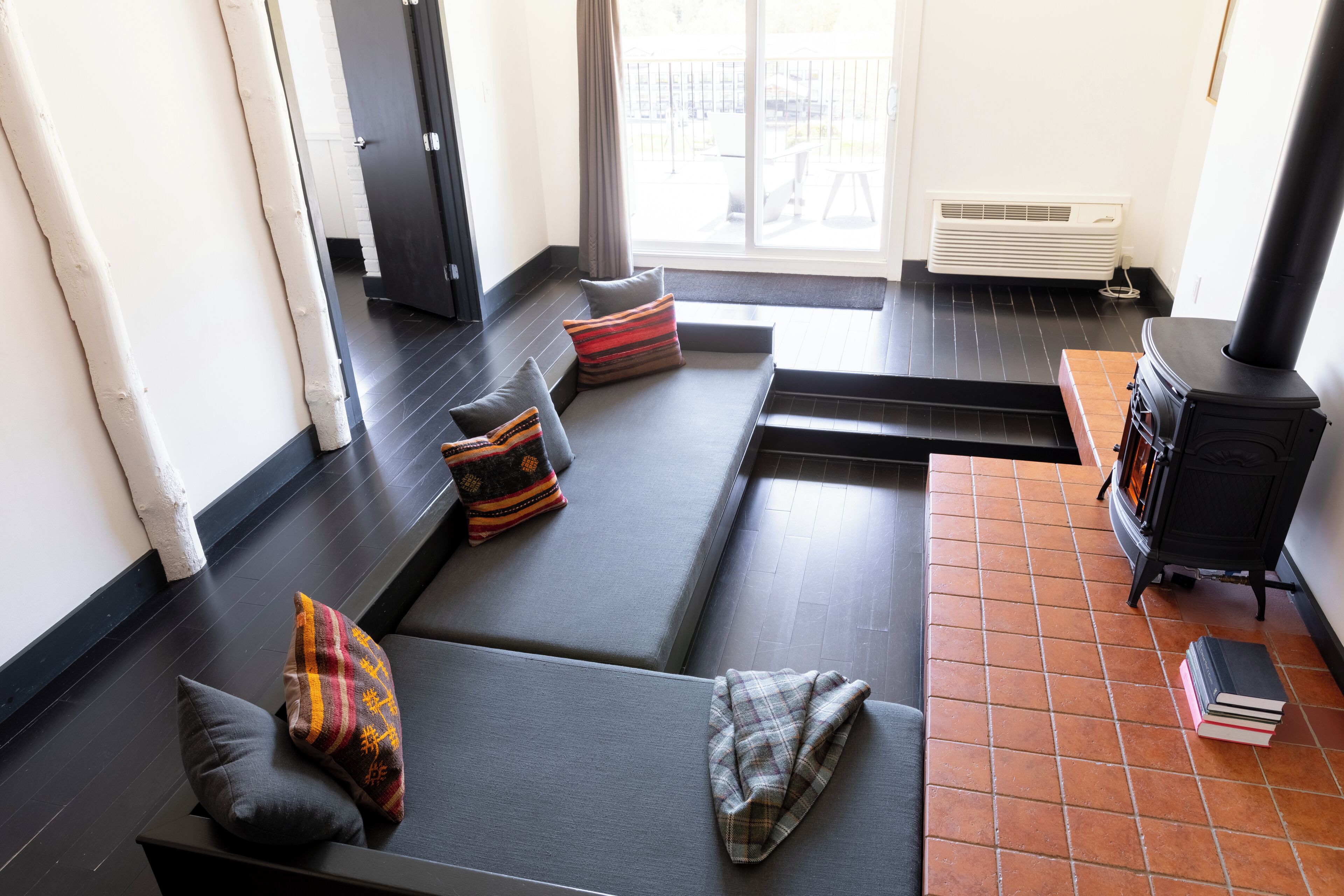 Un salon moderne avec un canapé noir, une cheminée et une vue à travers une porte vitrée.