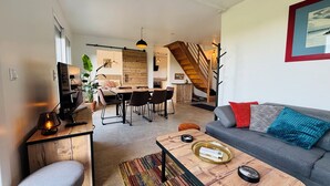 A modern living room with a gray sofa, a wooden coffee table, and a dining area with a wooden table and chairs. - Beautiful wooden house with 3-star rating (Beuzeville)