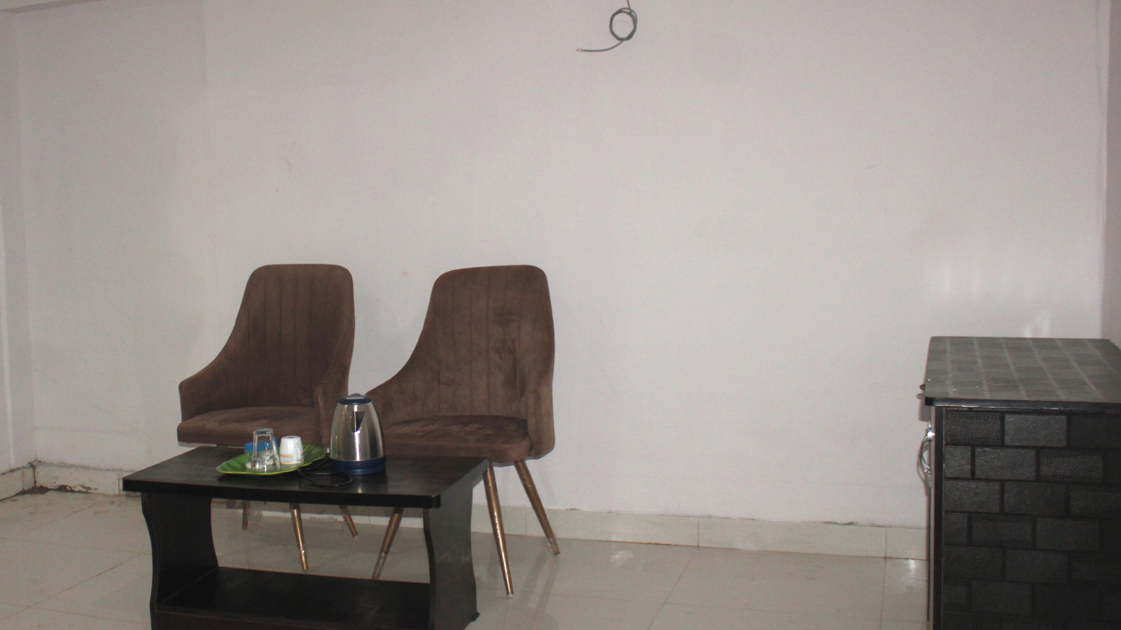 A room with two brown chairs, a small table with a tray, a kettle, and a small heater.