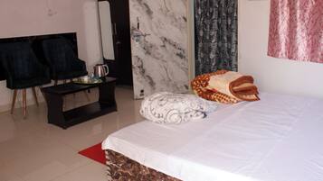 Quarto de hotel com cama, uma pequena mesa com chaleira, cadeiras, espelho e armário.