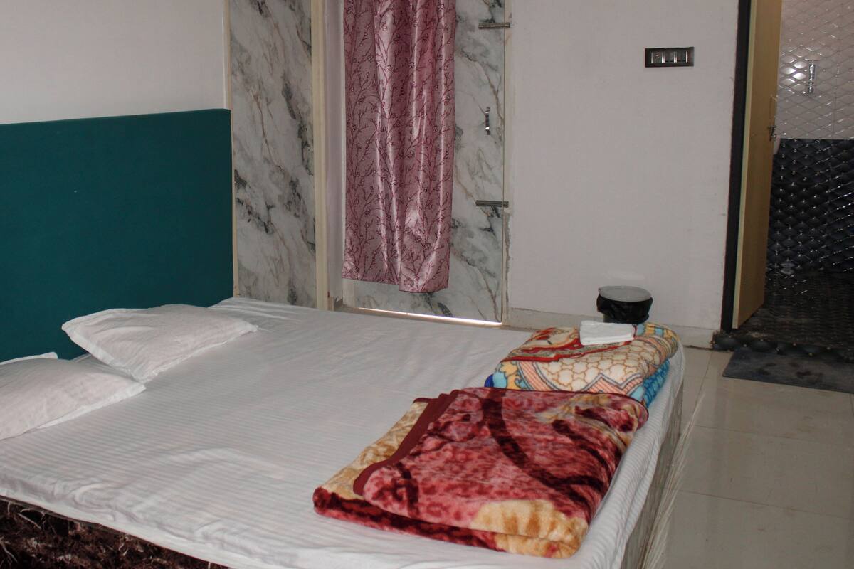 A bed with white linens, a teal headboard, a patterned blanket, and a marble wall.