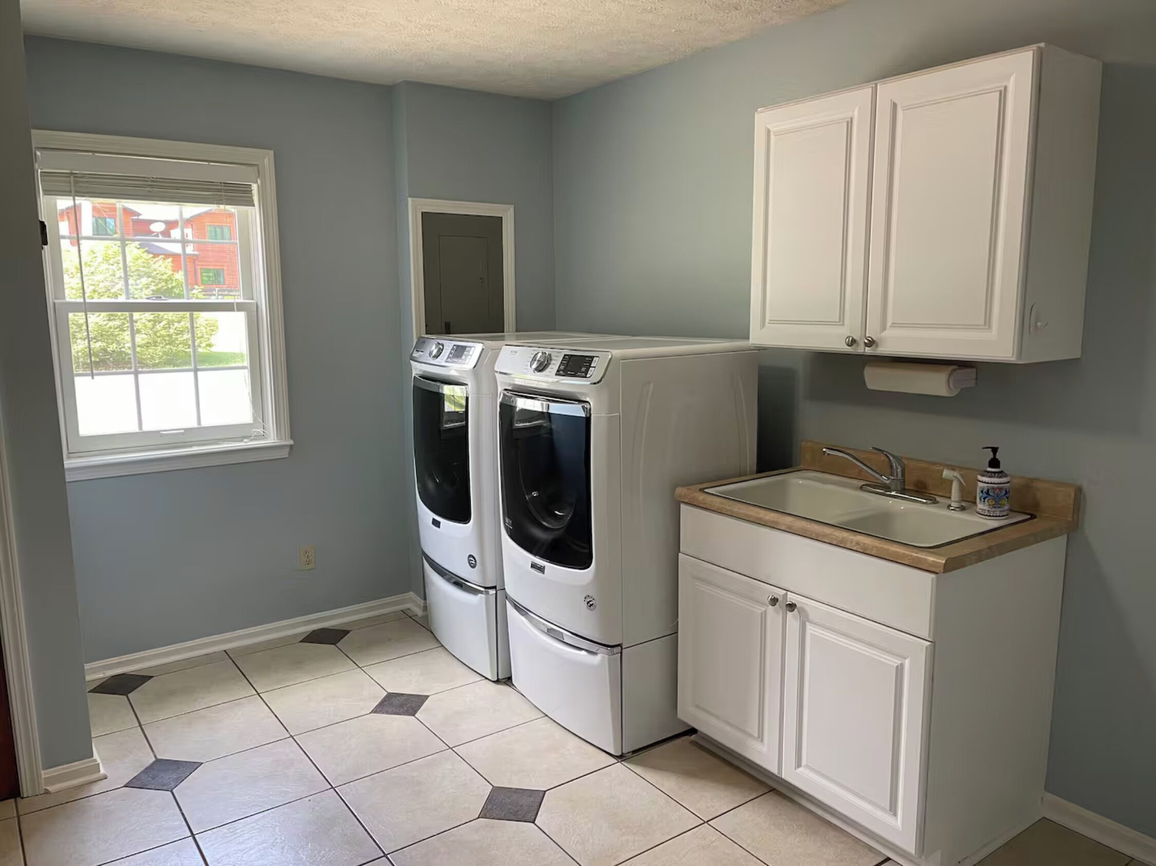 A laundry room with two front-loading washers and dryers, a sink with a wooden countertop, and white cabinetry.