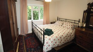 Een slaapkamer met een bed, nachtkastje, kapstok en een raam en deur.